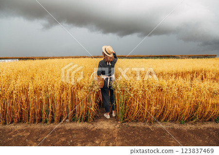 Girl in a wheat field wearing a straw hat on a cloudy day. Back view 123837469
