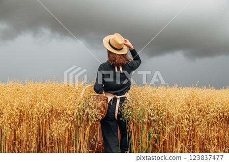Girl in a wheat field wearing a straw hat on a cloudy day. Back view 123837477