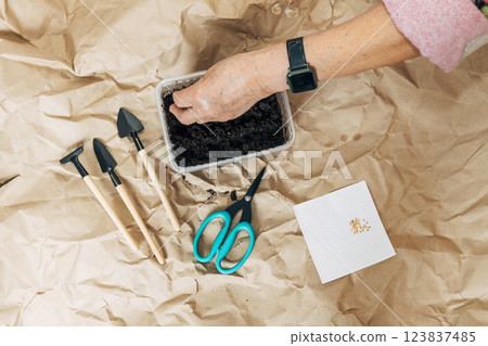 Kraft paper background, fertile soil and garden tools, top view. Hands planting seeds 123837485