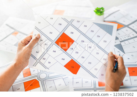 Woman holding a cadastral map looking at lots of lands. Land plot management - real estate concept with vacant land for building construction and housing subdivision for sale, rent, buy, or investment 123837502