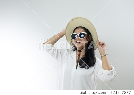 Beautiful young Asian woman tourist standing relaxation pose with sunglasses and hand holding straw hat on white background Beautiful young Asian woman tourist standing relaxation pose with sunglasses and hand holding straw hat on white background 123837877
