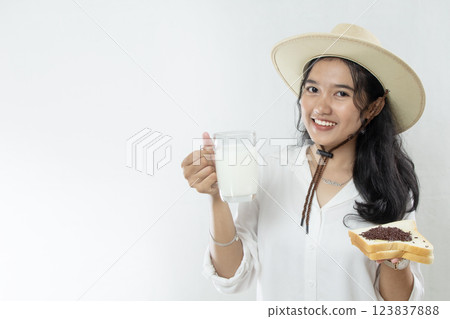 young woman in cowboy hat or beautiful dairy farm showing milk in her glass with one hand holding bread, isolated white background 123837888