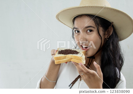 close up view of beautiful young Asian woman in straw hat and showing white bread with chocolate sprinkles smiling sweetly, isolated on white, breakfast healthy lifestyle 123838090