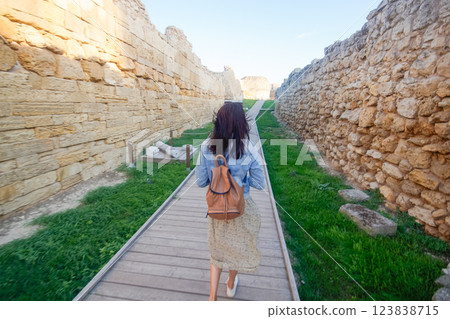 A woman tourist with a backpack walks and examines the ruins of an ancient city. Khersones, Sevastopol, Crimea. A woman tourist with a backpack walks and examines the ruins of an ancient city. Khersones, Sevastopol, Crimea. 123838715