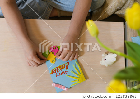 Child decorating a handmade Easter card with felt cutouts. 123838865