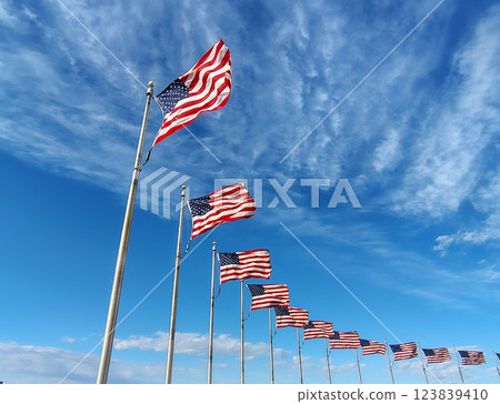 American flags on long flagpoles fluttering in the wind against a bright blue sky, national banners of the USA surrounding a monument, a symbol of the nation and state of the US 123839410