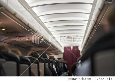Passage on the plane.Economy class interior, airplane cabin. The passengers are sitting in their seats. Transport safety. High quality photo Passage on the plane.Economy class interior, airplane cabin. The passengers are sitting in their seats. Transport safety. High quality photo 123839513