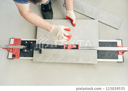 An installation for cutting large ceramic tiles into smaller tiles with precise dimensions. Close-up of the master cutting the tile into two parts with a machine. High quality photo 123839535
