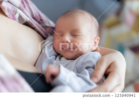 Newborn baby peacefully sleeping after breastfeeding in warm mother embrace at home. No face mother breastfeeding and hugging baby. Lactation infant concept. Baby eating milk before he sleeping. 123840941