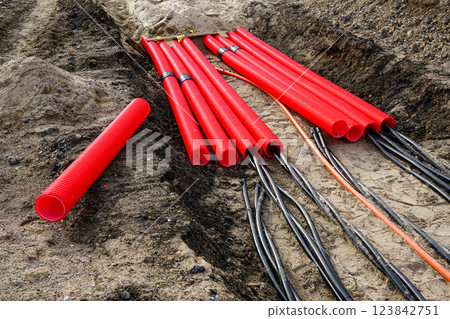 Laying new underground high-voltage power cable in red corrugated protective tube Laying new underground high-voltage power cable in red corrugated protective tube 123842751