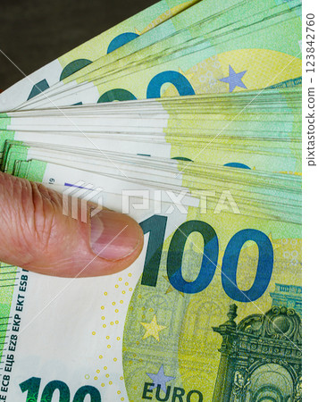 Cash in hand, thumb on a stack of 100 euro banknotes, concept of making profit, motivation to earn Cash in hand, thumb on a stack of 100 euro banknotes, concept of making profit, motivation to earn 123842760