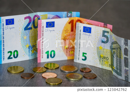 Five, ten and twenty euro banknotes and scattered coins on a gray background, low income concept 123842762
