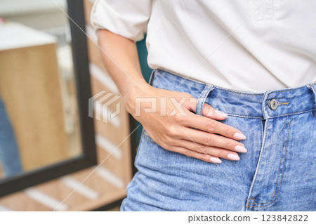 Female adjusting high waisted blue jeans wearing white blouse with polished 123842822