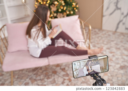 A woman is comfortably sitting on a pink couch while reading a book A woman is comfortably sitting on a pink couch while reading a book 123842883