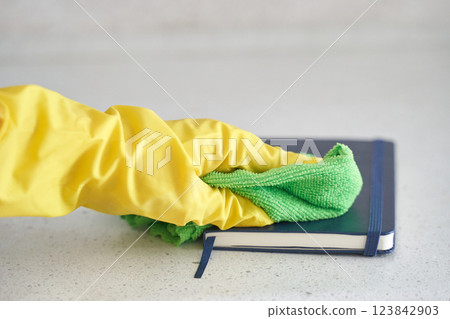 Gloved hand cleaning book with green cloth on light gray surface for hygienic Gloved hand cleaning book with green cloth on light gray surface for hygienic 123842903