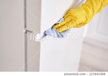 Gloved hand with yellow rubber glove cleaning white fridge door with blue cloth 123842906