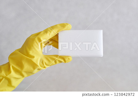 Close up of hand in yellow glove holding white cleaning sponge against neutral Close up of hand in yellow glove holding white cleaning sponge against neutral 123842972
