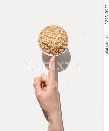 Caucasian adult hand pointing at bowl of brown rice on white background highligh 123843005