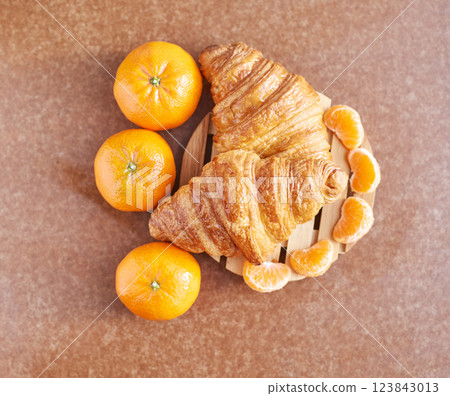 Delicious fresh croissants with vibrant oranges and sliced tangerines on wooden 123843013
