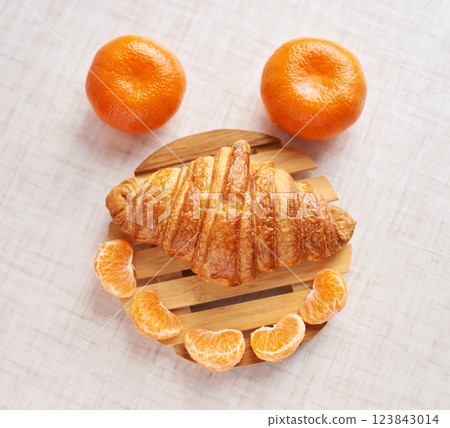 Creative breakfast arrangement with croissant and tangerines forming a smiley 123843014