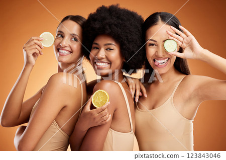 Diversity, beauty and friends, women and lemon for skincare, wellness and health on orange studio background. Smile, models and fruit, lemons or lime citrus for vitamin c, nutrition and healthy skin. 123843046