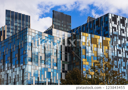 Modern glass buildings with reflective blue and gold facades in an urban cityscape Modern glass buildings with reflective blue and gold facades in an urban cityscape 123843455