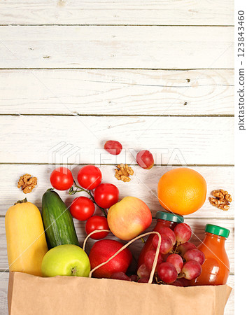 Grapes, oranges, tomatoes, apples, bananas and natural juice in a craft bag on a wooden background, food delivery concept, Paper eco bag with healthy vegan products for weight loss. Advertisement for Grapes, oranges, tomatoes, apples, bananas and natural juice in a craft bag on a wooden background, food delivery concept, Paper eco bag with healthy vegan products for weight loss. Advertisement for 123843460