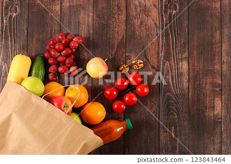 Grapes, oranges, tomatoes, apples, bananas and natural juice in a craft bag on a wooden background, food delivery concept, Paper eco bag with healthy vegan products for weight loss. Advertisement for Grapes, oranges, tomatoes, apples, bananas and natural juice in a craft bag on a wooden background, food delivery concept, Paper eco bag with healthy vegan products for weight loss. Advertisement for 123843464