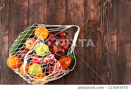 Fabric shopping bag with various vegan products for weight loss. Grapes, oranges, tomatoes, apples, bananas and natural juice in a cotton bag on a wooden background, food delivery concept, advertising Fabric shopping bag with various vegan products for weight loss. Grapes, oranges, tomatoes, apples, bananas and natural juice in a cotton bag on a wooden background, food delivery concept, advertising 123843470