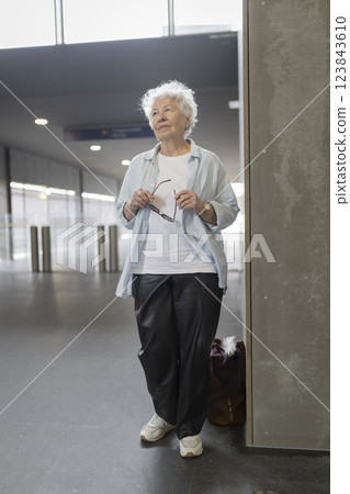 Senior woman waiting in airport terminal holding eyeglasses 123843610