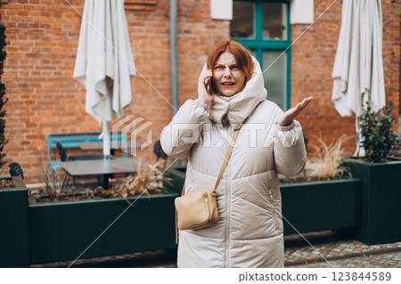 Angry woman on cell phone walking outside building. Frustrated woman talking on phone. Autumn time. Negative people emotion Angry woman on cell phone walking outside building. Frustrated woman talking on phone. Autumn time. Negative people emotion 123844589