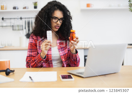 African woman in her 30s at desk researching medicine while attending online appointment 123845307