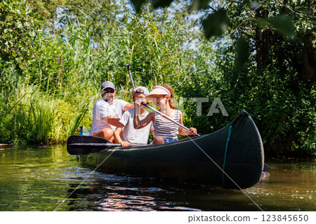 Man with two children enjoy having fun paddling canoe rent across lake river water wearing bright orange life vests hot sunny summer day. Healthy recreational activity lifestyle vacation trip journey 123845650