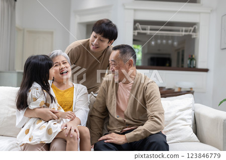 Grandmother, grandfather, and two younger family members are sitting on a couch engaging in lively conversation and sharing smiles. The atmosphere is warm and inviting. 123846779