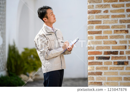 一名身著工作服的男子手持剪貼板，目視檢查一堵磚牆的場景 123847876