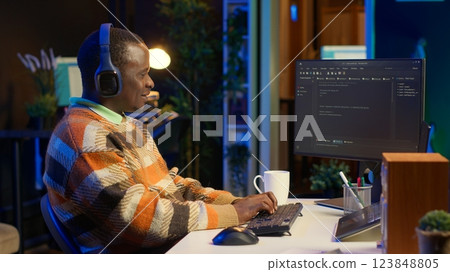 African american computer scientist in home office programming code on pc. Freelancing developer solving tasks for an IT job, writing lines of code at his personal office, cybersecurity. Camera A. 123848805