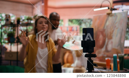 Woman artist hosting online class to present products and technique used on rustic artwork, recording tutorial online. Team of painters doing master class for e learning, art instruction. Camera B. Woman artist hosting online class to present products and technique used on rustic artwork, recording tutorial online. Team of painters doing master class for e learning, art instruction. Camera B. 123848898