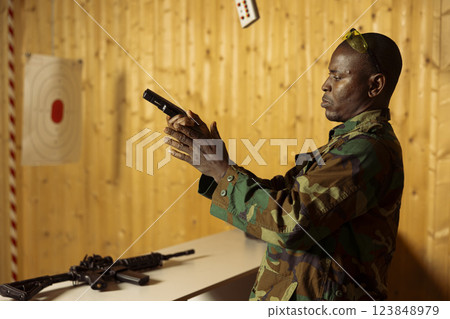 Man reloading firearm in shooting range used to train and test soldiers on necessary combat skills. Army soldier loading ammo magazine in pistol, training to enhance combat readiness 123848979