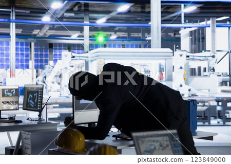 Masked hacker sneaking into solar panel plant at night, inserting USB stick into PC to steal confidential manufacturing data. Thief in photovoltaics facility extracts company files and uploading Masked hacker sneaking into solar panel plant at night, inserting USB stick into PC to steal confidential manufacturing data. Thief in photovoltaics facility extracts company files and uploading 123849000