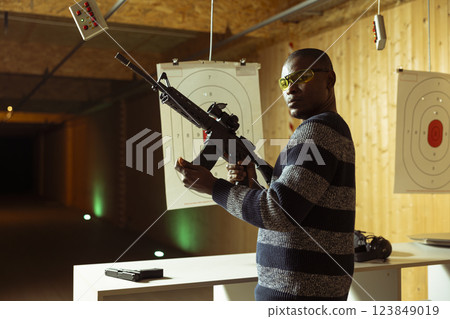 Portrait of shooting range client reloading rifle, preparing to shoot targets during leisure time. Man at indoor shooting ground facility loading semiautomatic weapon, wearing protection goggles Portrait of shooting range client reloading rifle, preparing to shoot targets during leisure time. Man at indoor shooting ground facility loading semiautomatic weapon, wearing protection goggles 123849019