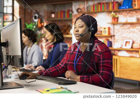 Teamworking call center colleagues in office helping customers by answering questions. Team of agents in customer support workplace in front of PC using headset mic to talk with clients 123849020