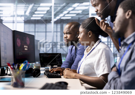 Team of engineers gathered together at PC in server farm to fight hacker passing firewall and stealing data. Critical error notification on monitor in data center scaring coworkers 123849069
