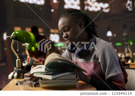 African american sleepy girl studying with exhaustion and burnout all night for exams, making preparations for a difficult school subjects. Young student consulting specialty books in the library. African american sleepy girl studying with exhaustion and burnout all night for exams, making preparations for a difficult school subjects. Young student consulting specialty books in the library. 123849119