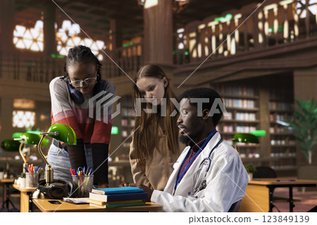 Multiethnic group of students in a library participate at a lesson with doctor, using medical books and materials to gain expertise in pharmacology and microbiology. Research for scientific studies. 123849139
