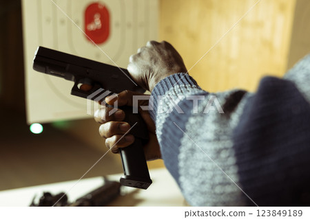 Gun hobbyist specialist in shooting range cocking handgun, setting mechanism up for firing, close up. African american person pulling back pistol hammer during training session, preparing to shoot Gun hobbyist specialist in shooting range cocking handgun, setting mechanism up for firing, close up. African american person pulling back pistol hammer during training session, preparing to shoot 123849189