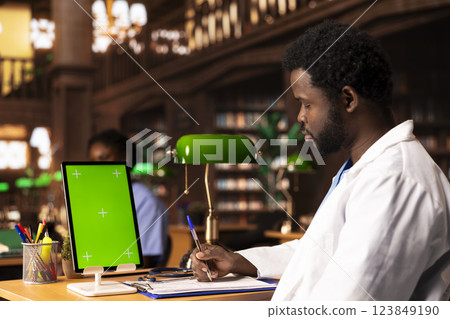 Future healthcare professional studying medical methods next to chroma key screen in an educational library, reading case files and academic papers. Black man works on academic growth. Future healthcare professional studying medical methods next to chroma key screen in an educational library, reading case files and academic papers. Black man works on academic growth. 123849190