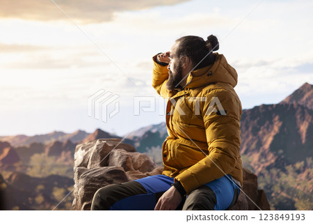 Trekker in warm clothing takes in the sweeping mountain scenic view, feeling the sense of freedom that comes with high altitude exploration. Nature lover enjoys fresh air and wilderness. 123849193