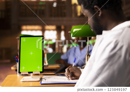 Black medical student examining class notes for research next to chroma key screen, studying new healthcare methods and practices for a successful career. Med school university pupil. Black medical student examining class notes for research next to chroma key screen, studying new healthcare methods and practices for a successful career. Med school university pupil. 123849197