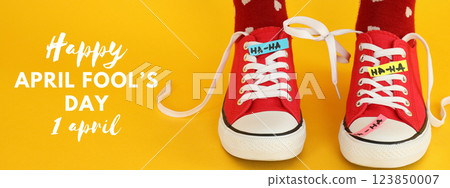 April Fool's Day, feet shod in red sneakers tied together, on a yellow background, with text 123850007