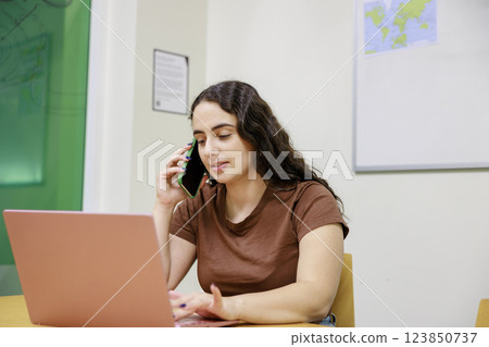 A woman talking on the phone while using a computer A woman talking on the phone while using a computer 123850737